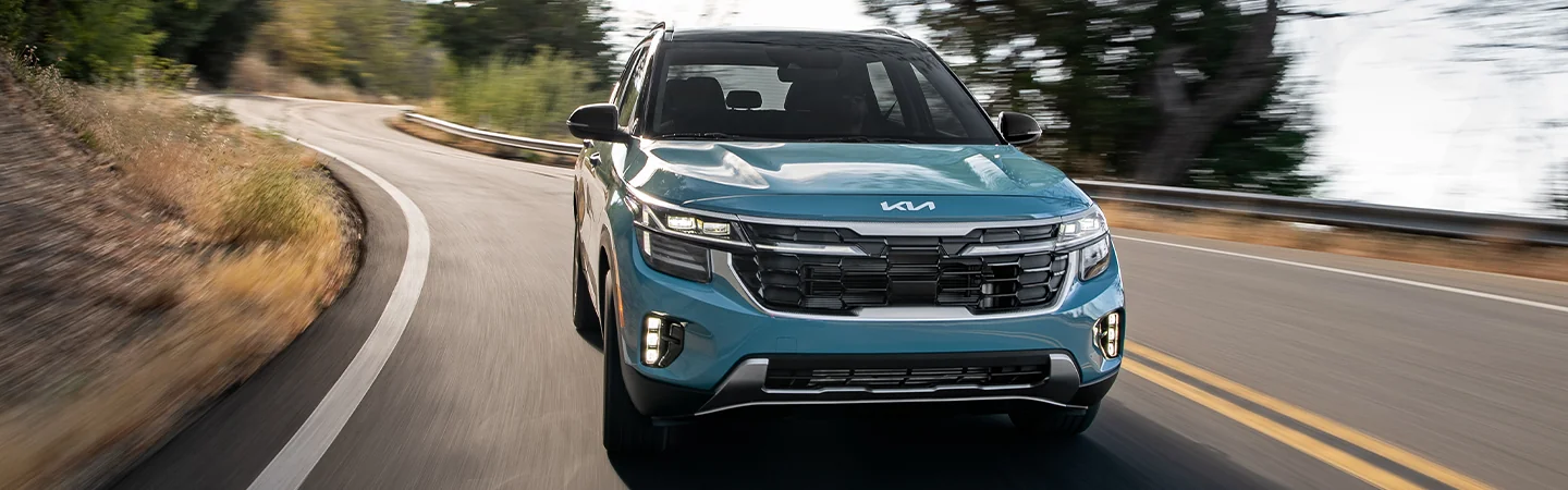 Front view of a blue 2025 Kia Seltos Specs driving on a road with trees around it