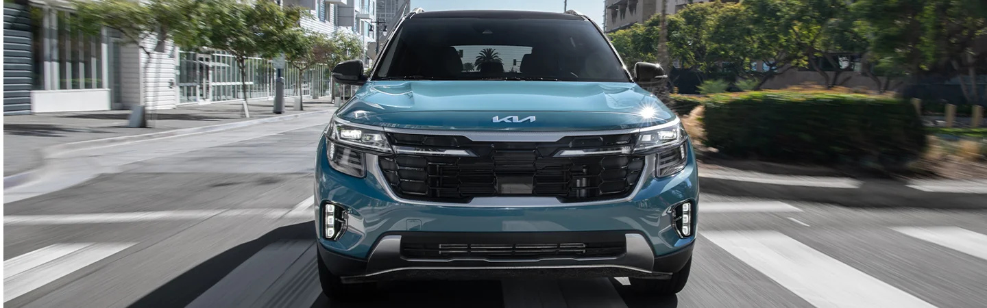 Front view of a blue 2025 Kia Seltos driving on a city street