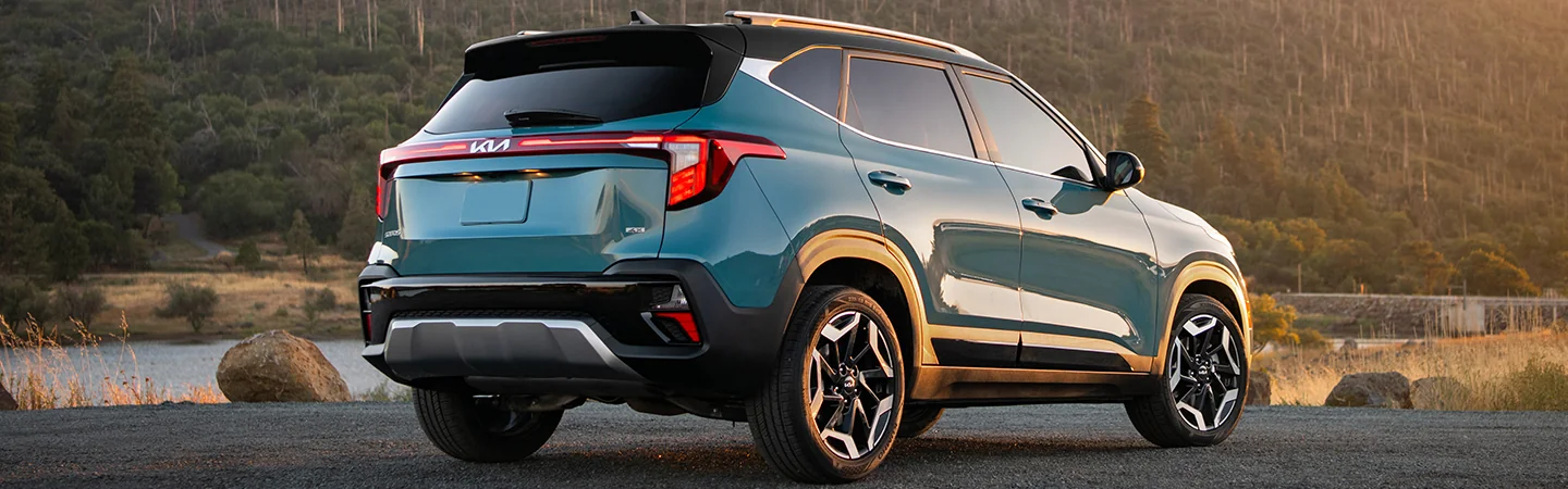 Back side view of a parked blue 2025 Kia Seltos at a lake next to a forest