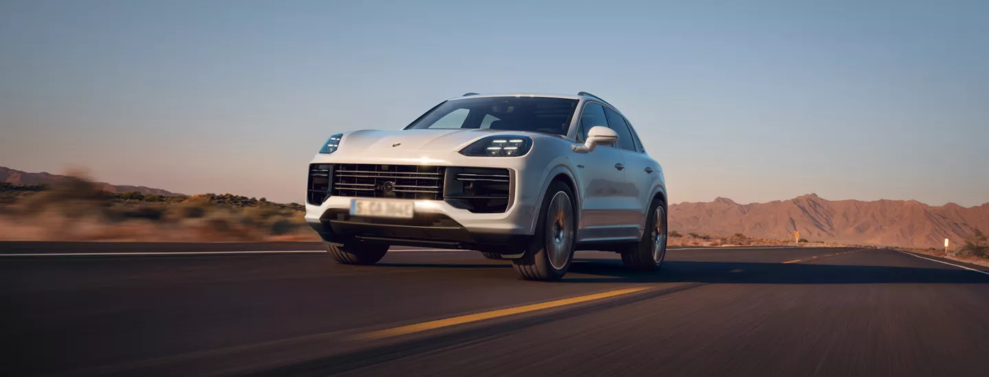 2026 Porsche Cayenne driving through a desert highway with mountains in the background