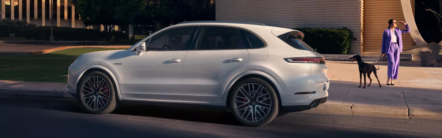2026 Porsche Cayenne side view parked near a residence with a woman and a dog in the background
