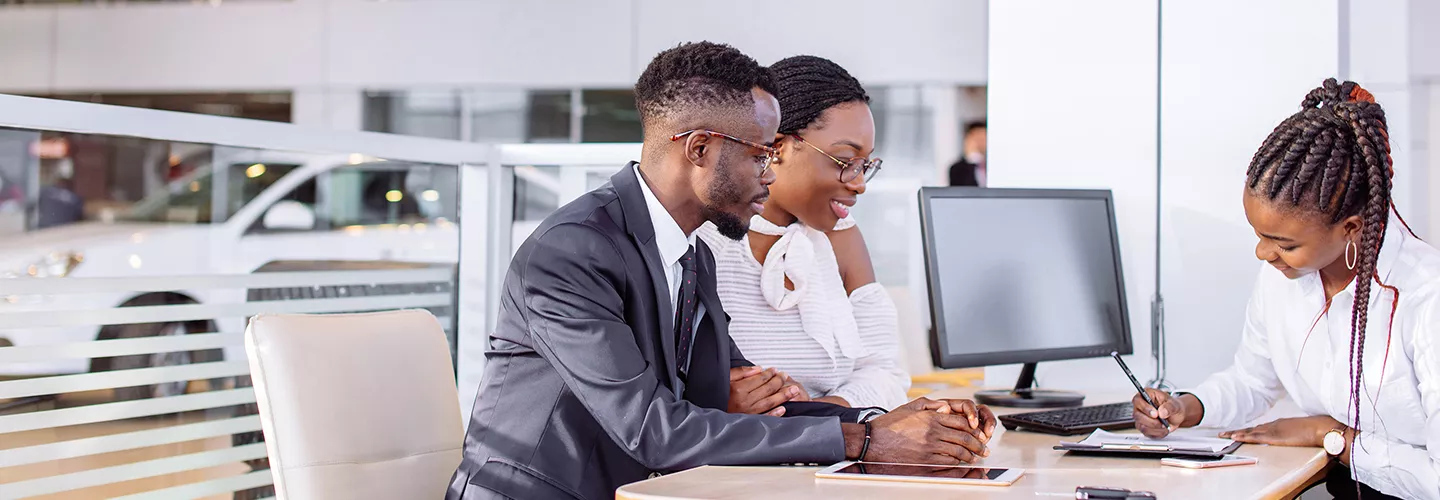 saleswoman going over documents on a tablet with a husband and wife in the dealership