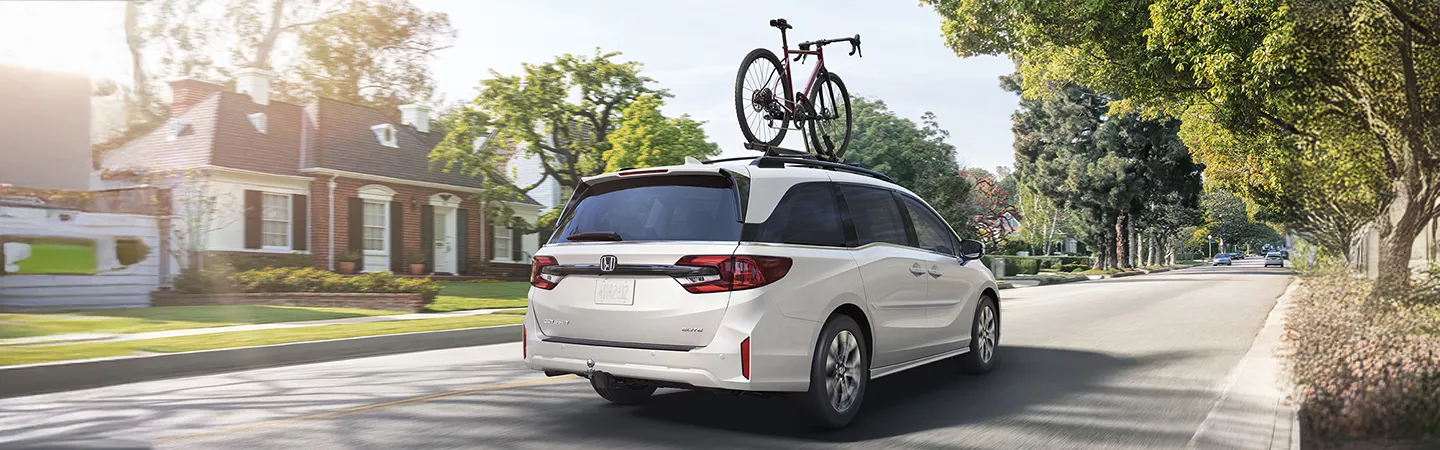 Rear view of the 2026 Honda Odyssey driving down the street with a bike on the roof rack