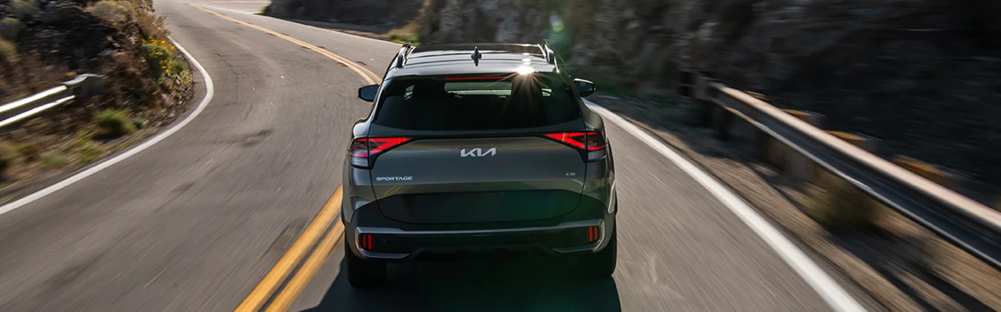 Back view of a 2025 Kia Sportage driving on a mountain road
