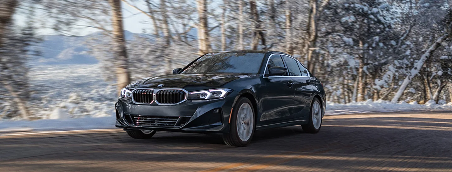 front view of a black 026 BMW 3 Series driving on a snowy day