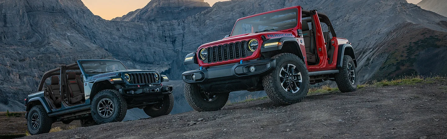 Two 2026 Jeep Wrangler parked on a rocky hill with mountains in the background