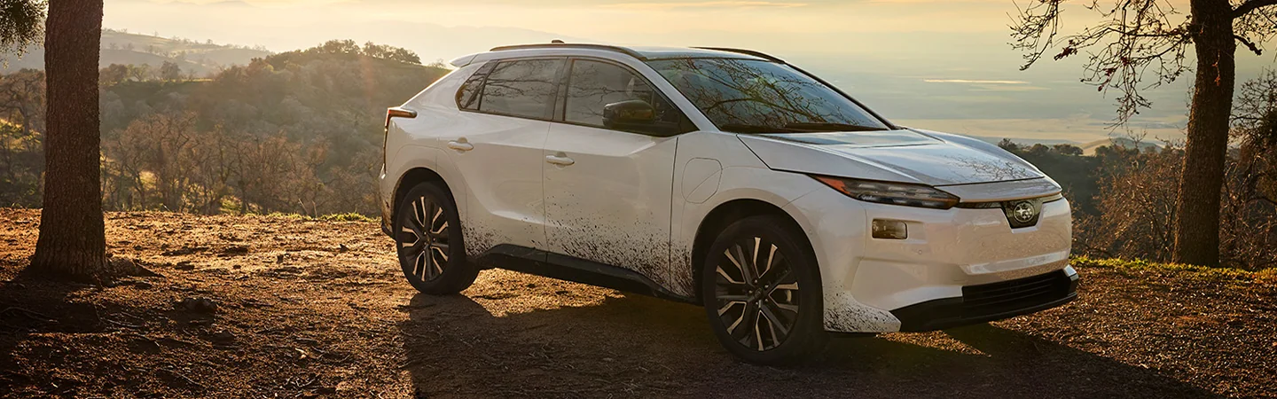 Side view of a parked white 2026 Subaru Solterra on a wooded cliff side