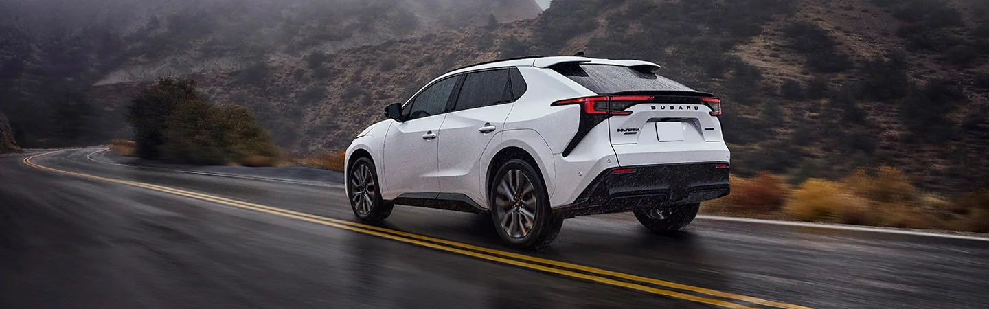 Back side ivew of a white 2026 Subaru Solterra driving on a mountain road