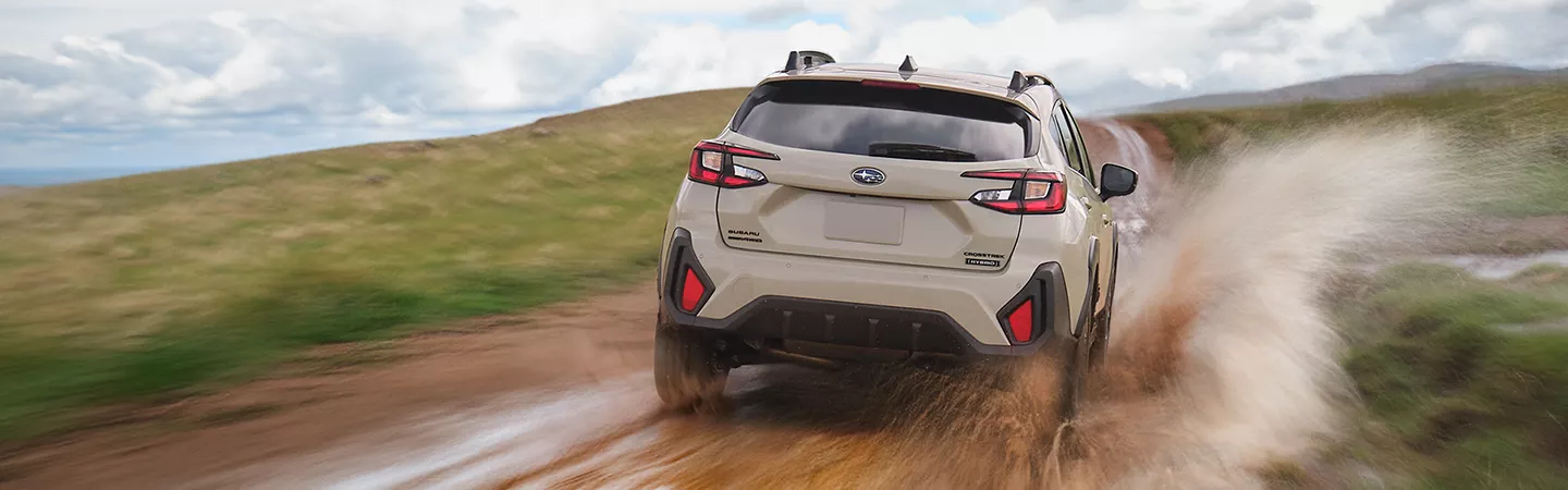 Rear view of 2026 Subaru Crosstrek driving through a mud puddle with grassy hills in the background in Leesburg, FL