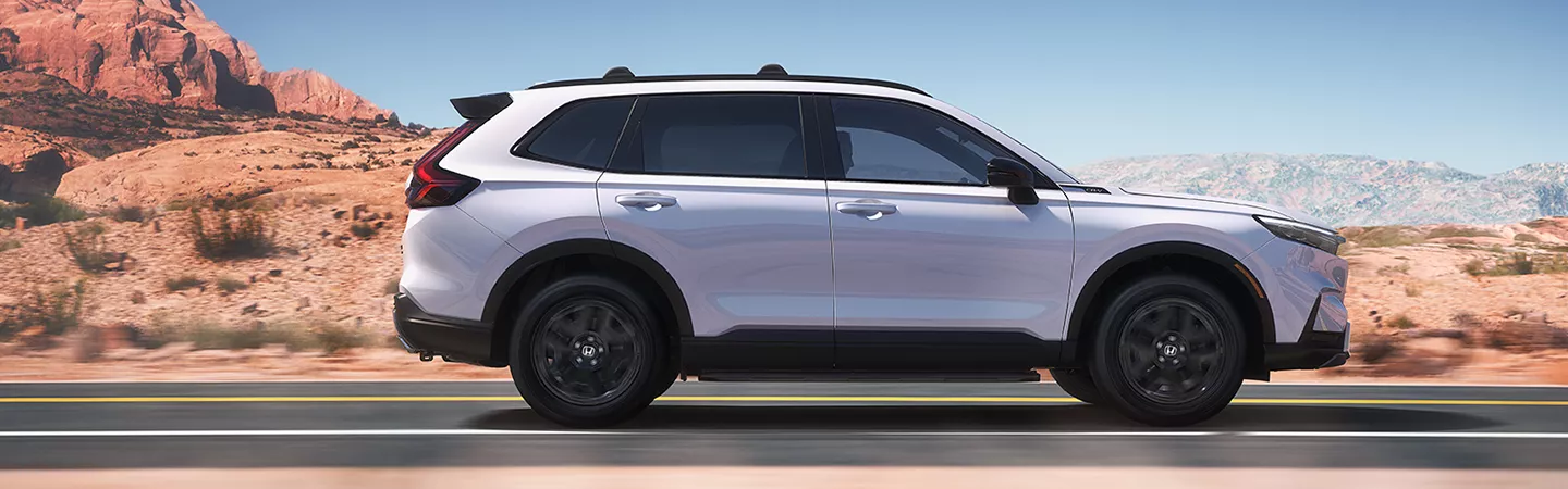 Side view of the 2026 Honda CR-V driving on a highway with desert mountains in the background