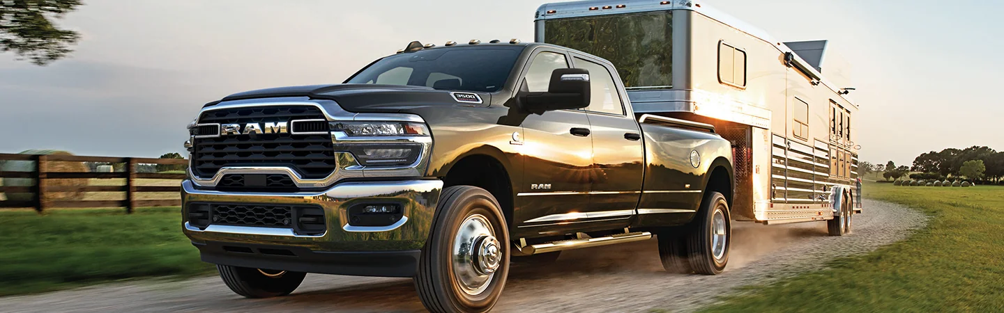 Front view of a black 2026 RAM 3500 pulling a trailer on a farm