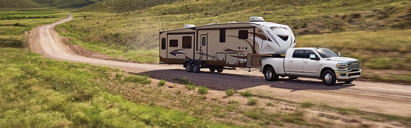 Side view of a gray 2026 RAM 3500 pulling a trailer on a dirt road