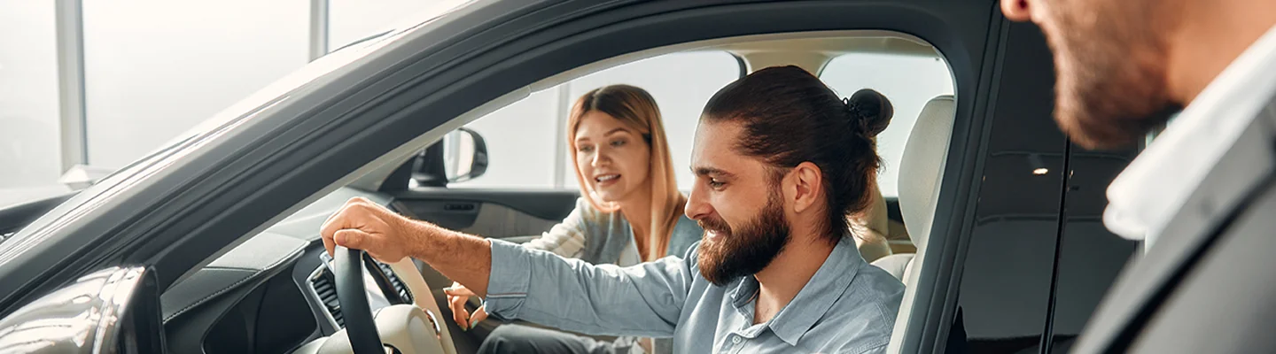 a couple seated in a car in showroom smiling