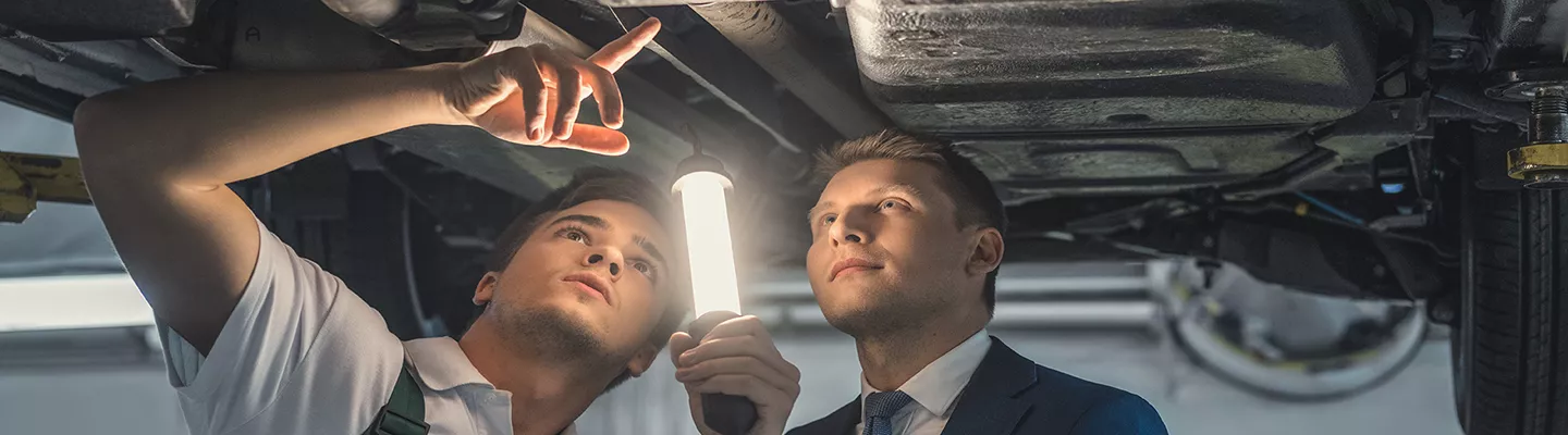 mechanic showing guy in suit the issue under the vehicle