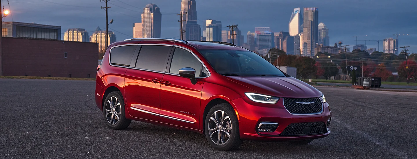 Side view of a parked red 2026 Chrysler Pacifica with a city in the background