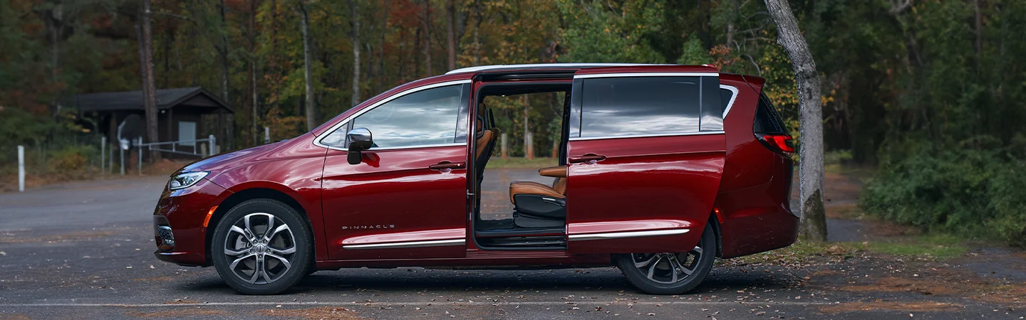 Side view of a parked red 2026 Chrysler Pacifica with the sliding doors open at a park