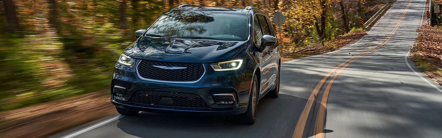 Frotn view of a blue 2026 Chrysler Pacifica driving though the woods
