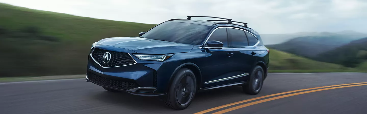 2026 Acura MDX driving on a country road with hills in the background