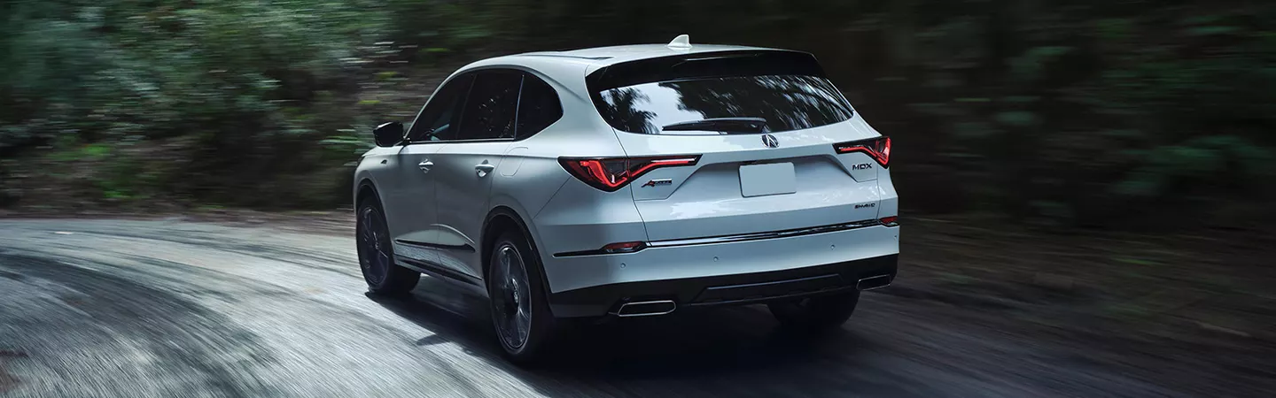 Rear view of 2026 Acura MDX driving on a country road with trees in the background