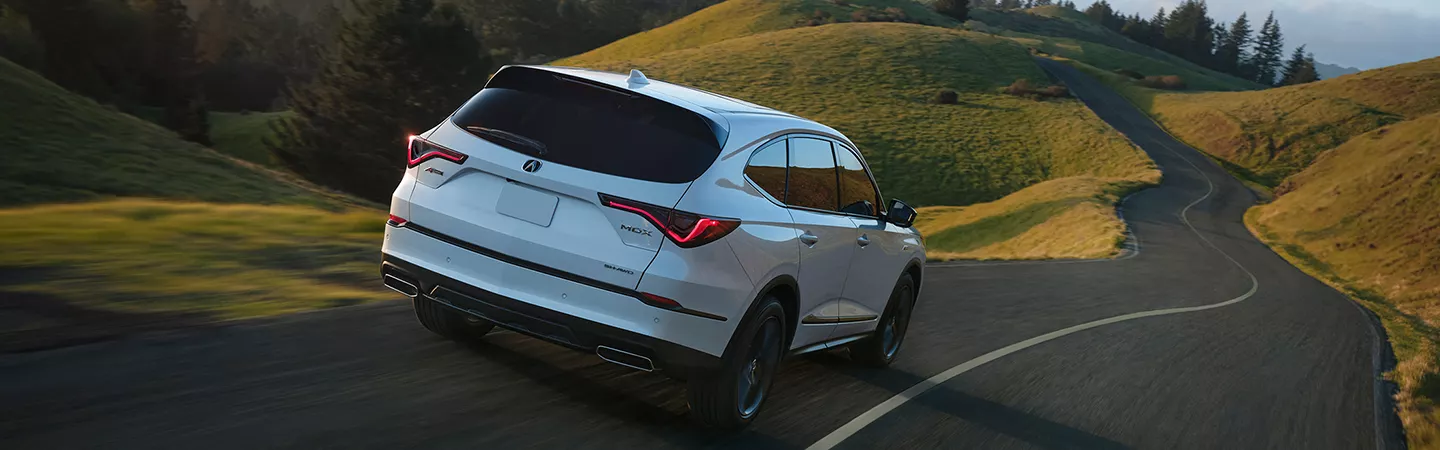 2026 Acura MDX driving on a country road with hills and trees in the background