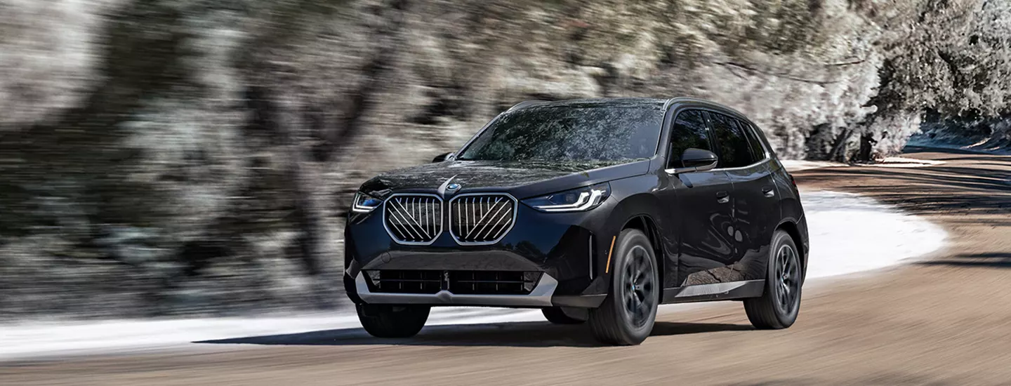 2026 BMW X3 driving on a country road with snowy trees in the background