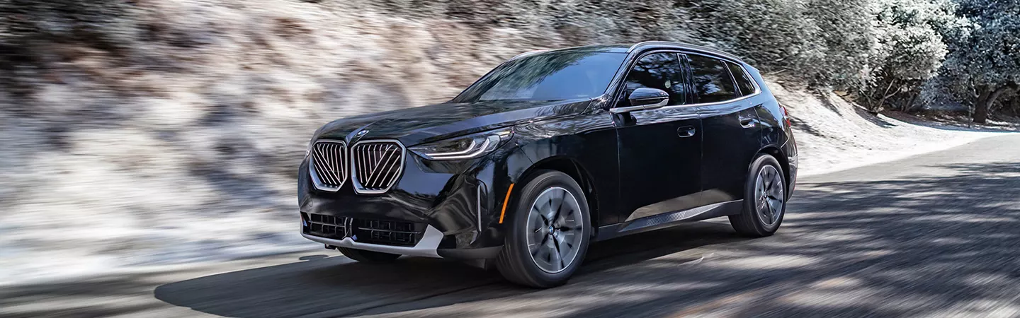 2026 BMW X3 30 xDrive driving on a country road with snowy trees in the background