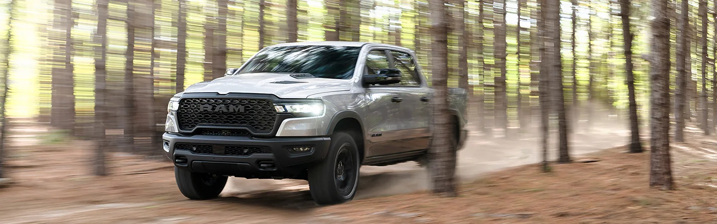 Front view of a gray 2026 RAM 1500 driving in the woods