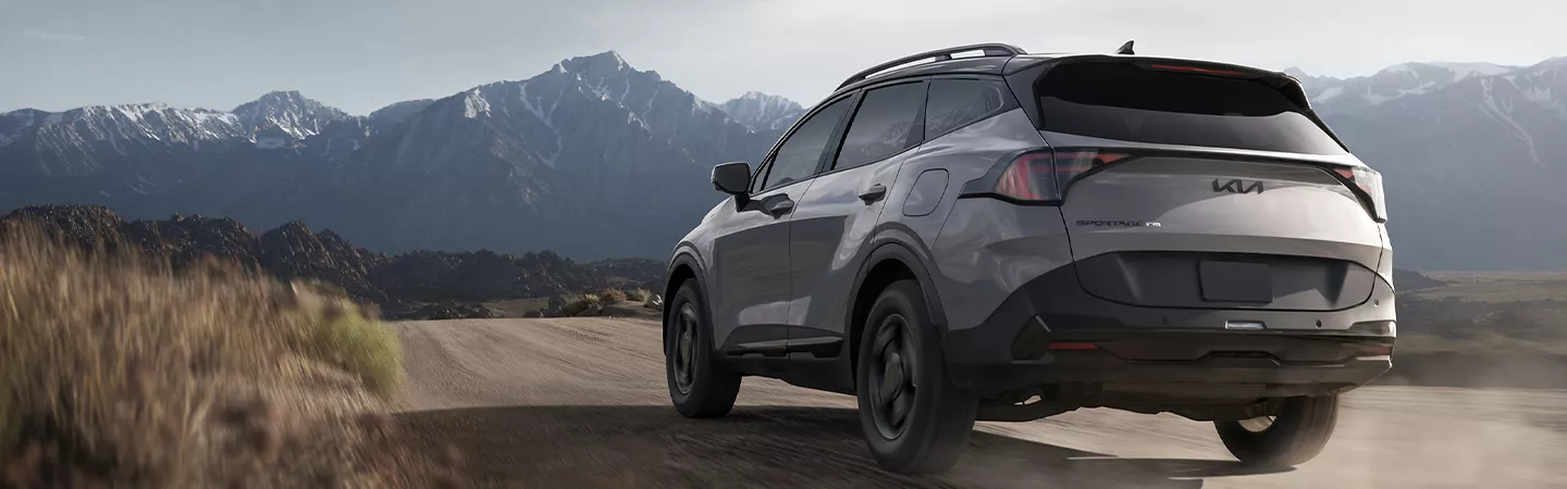 Rear view of the 2026 Kia Sportage driving toward the mountains on a dirt road