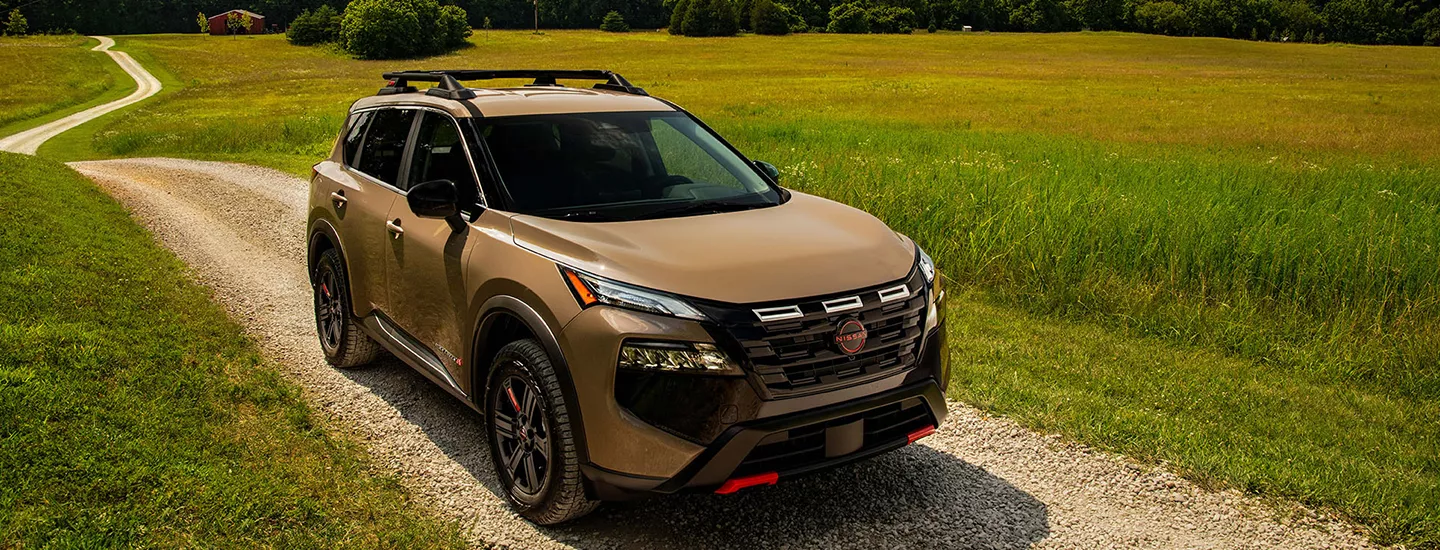 2026 Nissan Rogue driving on a country road with grass in the background
