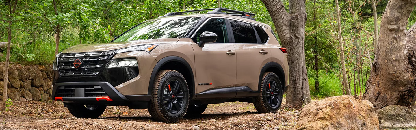2026 Nissan Rogue driving on a country road with trees and rock walls in the background