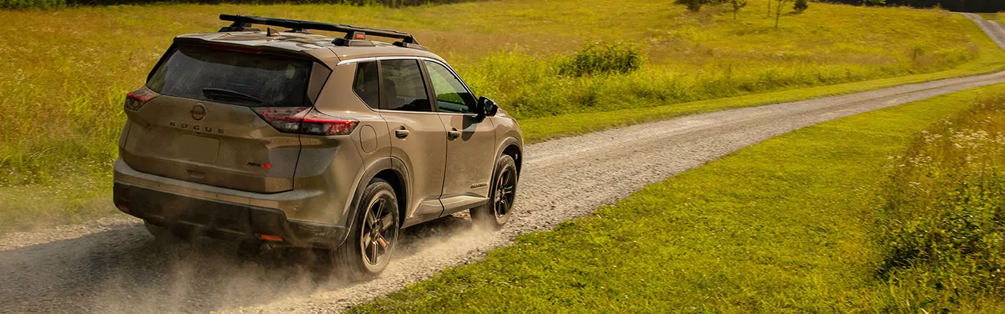 Rear view of the 2026 Nissan Rogue driving on a country road