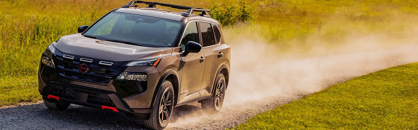 Front view of the 2026 Nissan Rogue driving on a country road with dust kicking up from the tires