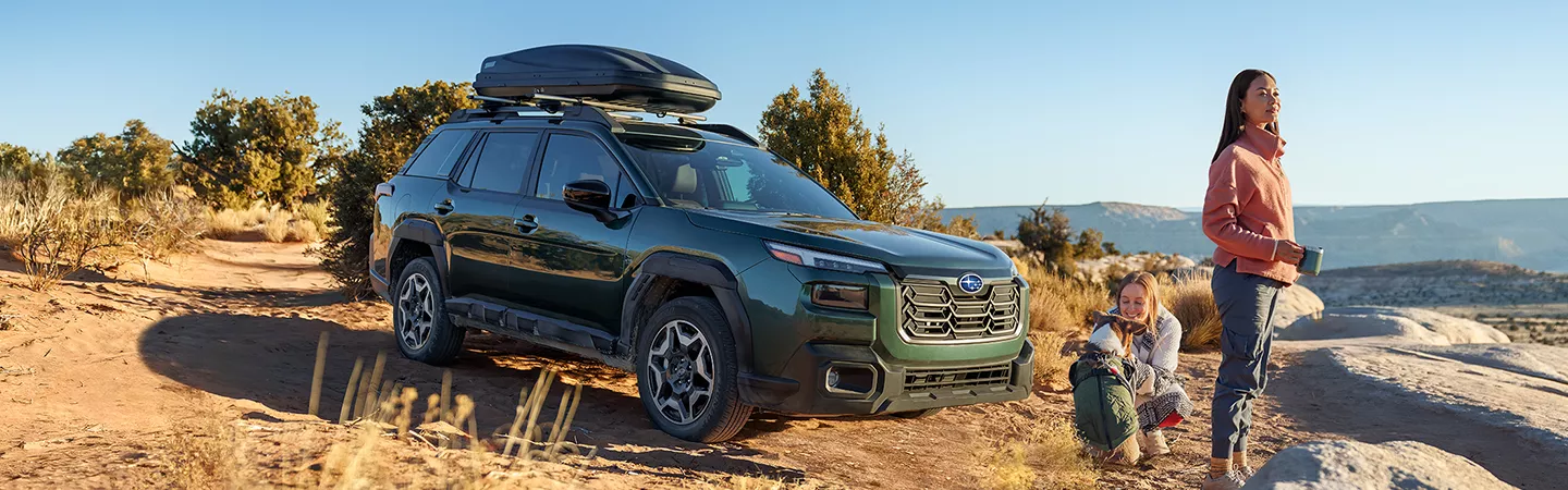 2026 Subaru Outback parked at a desert mountain overlook with people and a dog standing next to it