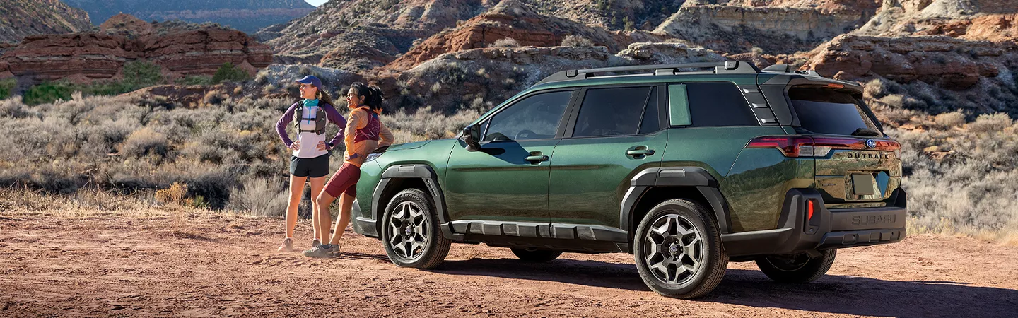Hikers standing next to a 2026 Subaru Outback in a desert mountain setting