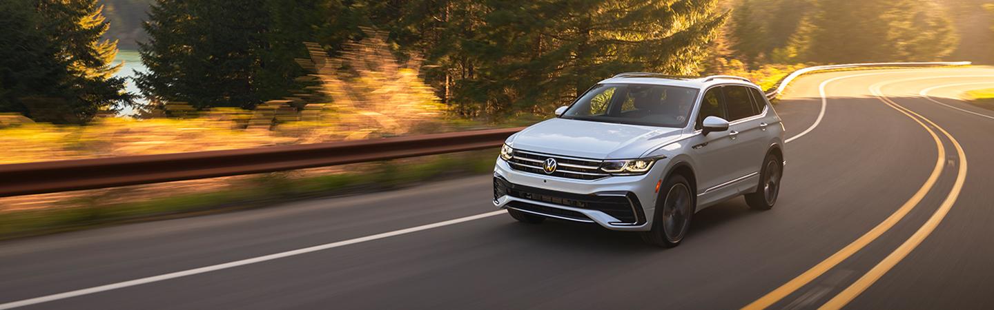 Gray 2022 Volkswagen Tiguan driving on a road by woods and a lake