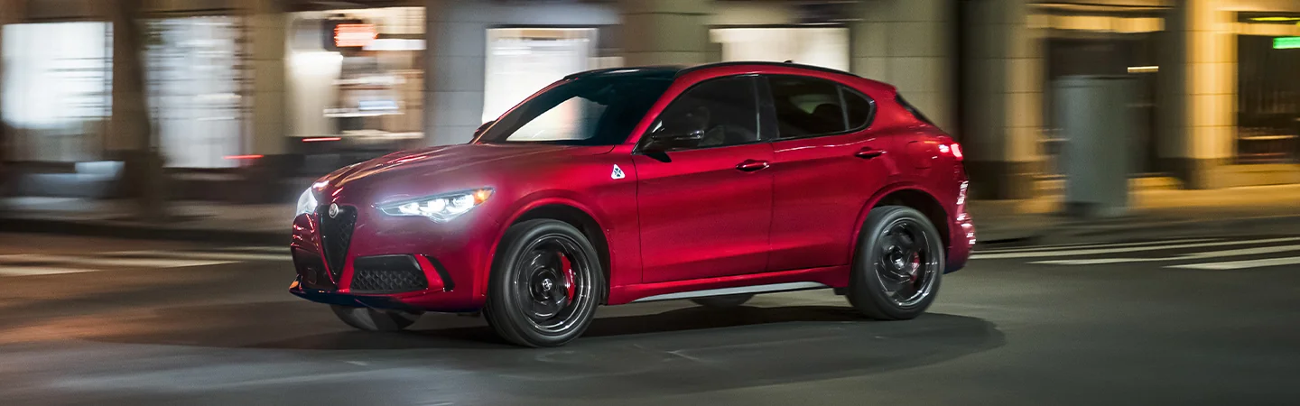 Side view of a red 2025 Alfa Romeo Stelvio in motion in a city
