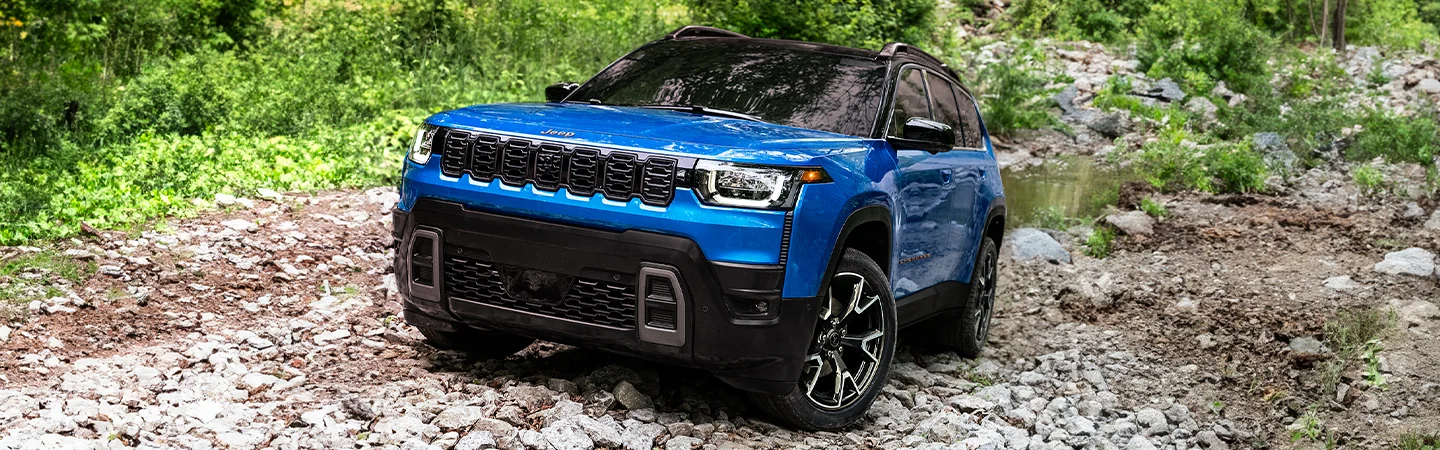 Front view of a blue 2026 Jeep Cherokee parked on a rocky hill