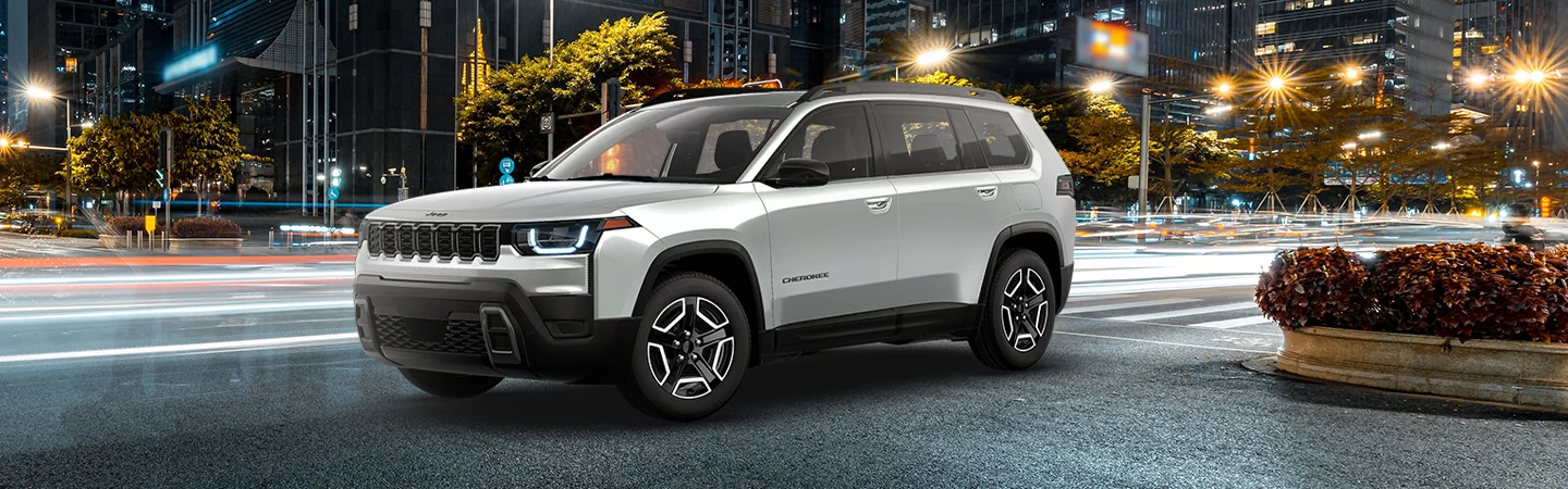 Front side view of a gray 2026 Jeep Cherokee with a city in the background
