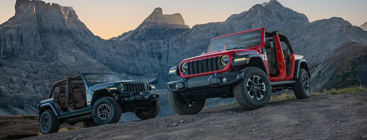Two 2026 Jeep Wranglers parked in front of desert mountains at sunset