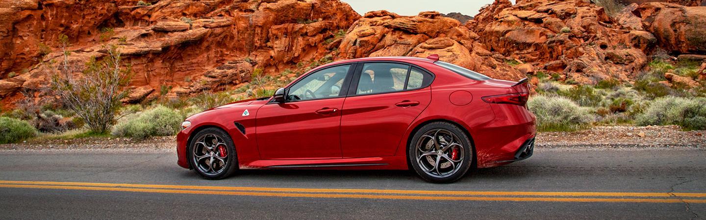 Side view of a red 2021 Alfa Romeo Giulia parked in the desert.