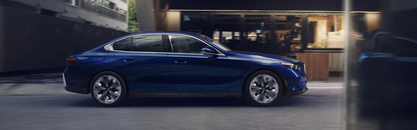 Side view of a blue 2025 BMW 5 Series driving on a city street