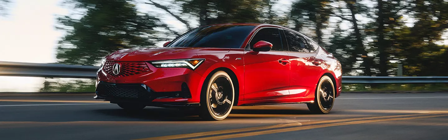 Side view of a red 2026 Acura Integra driving on a country road