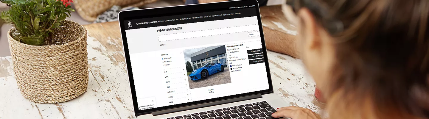 woman sitting at a table looking at her laptop at the Inventory feed of Lambo Sarasota