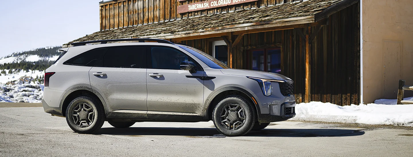 Side view of a parked gray 2025 Kia Sorento at a store in snowy landscape