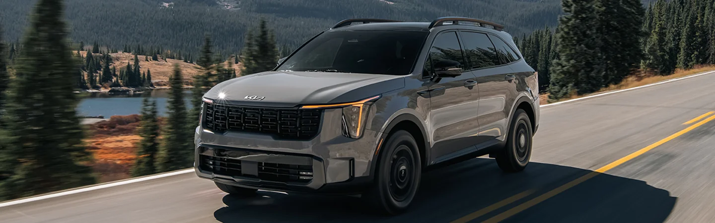 Front side view of a gray 2025 Kia Sorento driving by a lake and a forest