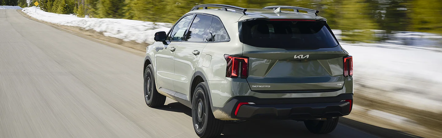 Back view of a 2025 Kia Sorento driving on a road next to a snowy landscape