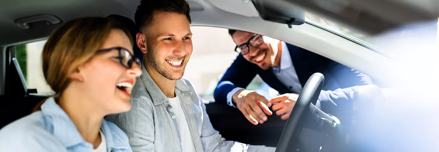 salesman pointing to the dash to a couple who are sitting in the car