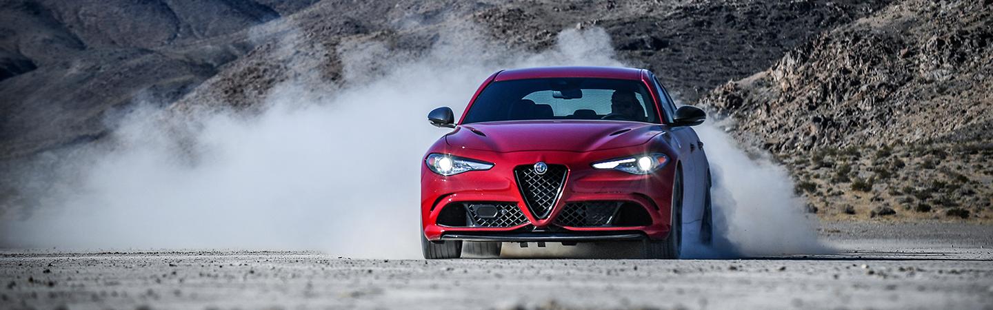 Front view of a red 2021 Alfa Romeo Giulia Quadrifoglio kicking up dust.