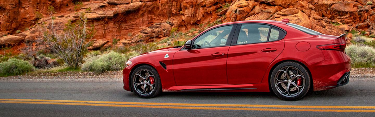 Side view of a red 2021 Alfa Romeo Giulia Quadrifoglio parked in the desert.