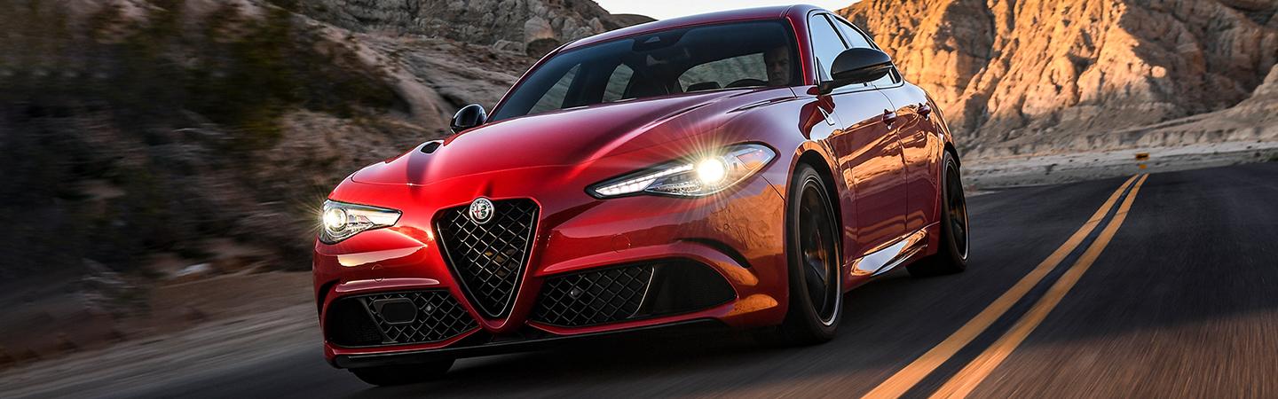 Close-up of the front of a red 2021 Alfa Romeo Giulia Quadrifoglio driving down the road.